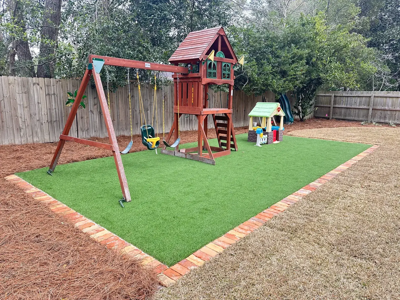 Backyard synthetic turf play area with brick edging and playset in Valdosta GA
